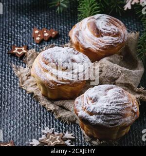 Croccini moderni per pasticceria, come croissant e muffin con zucchero in polvere, serviti con decorazioni natalizie e abeti su fondo di tessitura scura. Clos Foto Stock