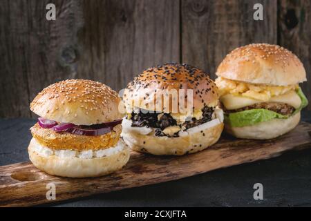 Tre hamburger di verdure fatti in casa con patate dolci, riso nero e fagioli rossi, serviti su trivella di legno su sfondo nero testurizzato. Foto Stock