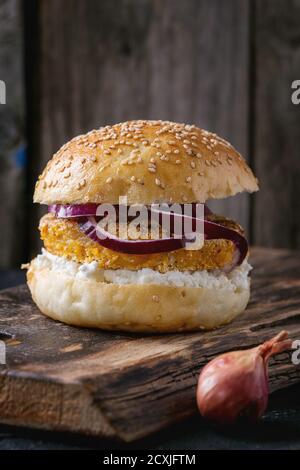 Hamburger vegetariano fatto in casa con patate dolci, formaggio casereccio e cipolla rossa, servito su trivella di legno su vecchio sfondo di legno. Stile rustico Foto Stock