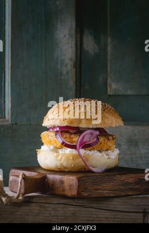 Hamburger vegetariano fatto in casa con patate dolci, formaggio casereccio e cipolla rossa, servito su trivella di legno su vecchio sfondo di legno. Stile rustico Foto Stock