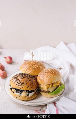 Tre hamburger di verdure fatti in casa con patate dolci, riso nero e fagioli rossi, serviti su piatto bianco con asciugamano da cucina su fondo testurizzato bianco. Foto Stock