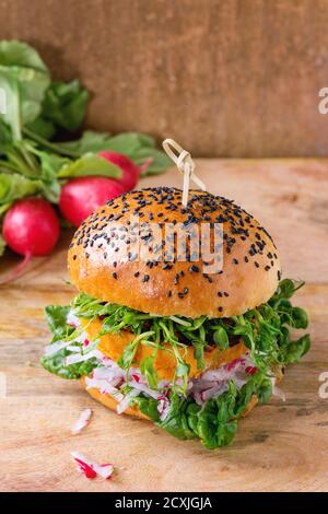 Hamburger di patate dolci veggie fatti in casa con ravanelli e germogli di piselli freschi serviti con un mazzo di ravanelli su sfondo testurizzato in legno. Foto Stock