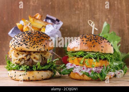 Hamburger tradizionali e veggie fatti in casa con manzo, cipolla fritta, patate dolci, ravanello e germogli di piselli, serviti su sfondo testurizzato in legno. Sano Foto Stock