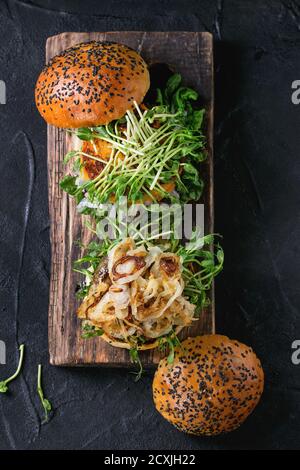 Hamburger tradizionali e veggie fatti in casa con manzo, cipolla fritta, patate dolci, ravanello e germogli di piselli, serviti su sfondo testurizzato in legno. Sano Foto Stock