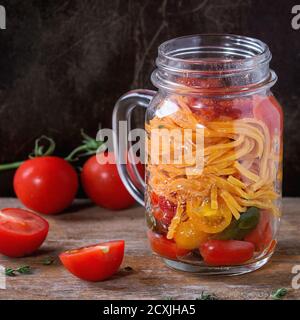 Pasta di pomodoro con salsa, timo e pomodori ciliegini a fette in vasetto di vetro di muratore, servita su vecchio sfondo di legno scuro. Pranzo da andare. Immagine quadrata Foto Stock