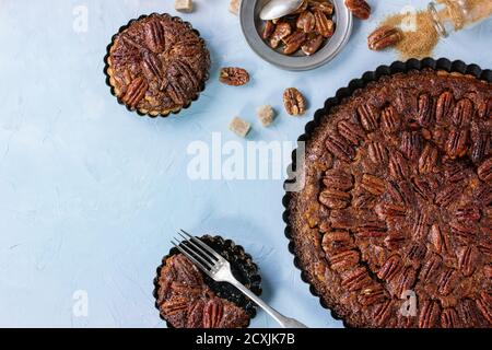 Torta di pecan al caramello grande e rotonda fatta in casa e piccole tartine in ferro nero, servite con zucchero di canna, salsa al caramello e posate vintage su testo blu Foto Stock