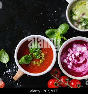 Varietà di zuppe vegetariane fredde gazpacho cetriolo con menta, barbabietola con formaggio feta, pomodoro con pesto verde, servito con condimento in tazze sopra b Foto Stock