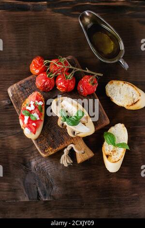 Varie bruschette con pomodori, fragole, formaggio feta, pollo, funghi e basilico su baguette tostate, servite con olio d'oliva su taglie di legno Foto Stock