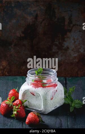 Vaso di vetro quadrato con yogurt fatto in casa con purea di menta e fragola, servito con frutti di bosco freschi su sfondo di legno scuro. Con spazio per il testo. Foto Stock