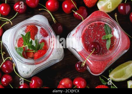 Due vasetti di vetro quadrati con yogurt fatto in casa con menta, purea di fragole, ciliegia e semi di chia serviti con frutti di bosco freschi e lime affettato su woo scuro Foto Stock