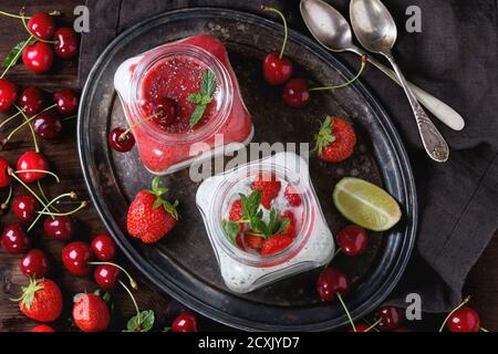 Due vasetti di vetro quadrati con yogurt fatto in casa con menta, purea di fragole, ciliegia e semi di chia serviti su vassoio vintage con frutti di bosco freschi e li affettati Foto Stock