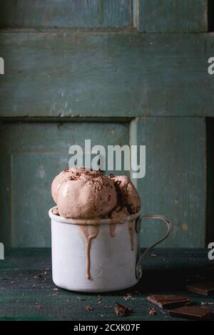 Tazza di alluminio vintage surgelata con palle di gelato al cioccolato fondente, servita con cioccolato fondente tritato su vecchio tavolo di legno. Stile rustico scuro. Spazio f Foto Stock