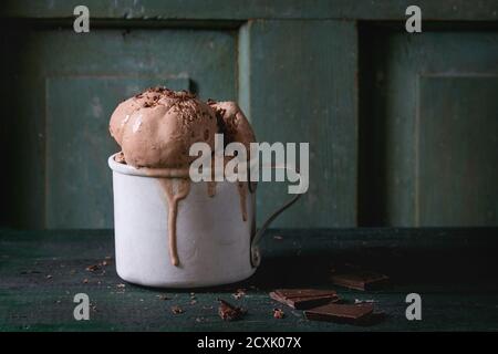 Tazza di alluminio vintage surgelata con palle di gelato al cioccolato fondente, servita con cioccolato fondente tritato su vecchio tavolo di legno. Stile rustico scuro. Spazio f Foto Stock