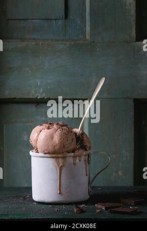 Tazza di alluminio vintage surgelata con palle di gelato al cioccolato fondente, servita con cucchiaio e cioccolato fondente tritato su vecchio tavolo di legno. Stile rustico scuro Foto Stock