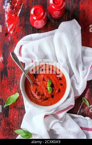 Piastra bianca di freddo fresco di pomodoro Zuppa Gazpacho con basilico e balsamico, servita con rosso sale e pepe bianco su carta asciugatutto su rosso e bl Foto Stock