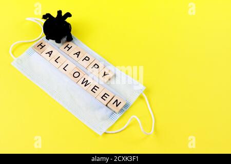 Ragno giocattolo nero, maschera medica e parole felici Halloween sul giallo. Halloween decorazione di fondo concetto di vacanza Foto Stock