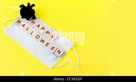Ragno giocattolo nero, maschera medica e parole felici Halloween sul giallo. Halloween decorazione di fondo concetto di vacanza. Spazio di copia. Banner Foto Stock