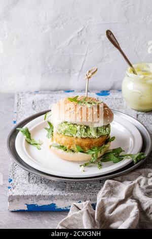 Hamburger vegetariano con cipolla e cotolette di formaggio, insalata di avocado, rucola e salsa allo yogurt in piatto bianco su fondo grigio a trama di pietra. Sano Foto Stock