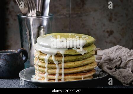 Pila di frittelle dolci americano ombre tè verde con salsa di latte condensata a flusso servita su un piatto grigio con brocca di panna e posate su b Foto Stock