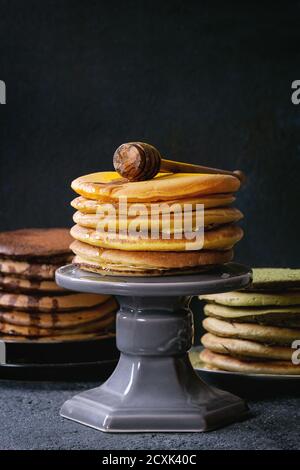 Varietà di fatti in casa american ombre cioccolato, tè verde Matcha e curcuma frittelle con miele e salsa servita su piatti e una fetta di torta in piedi sopra il nero s Foto Stock