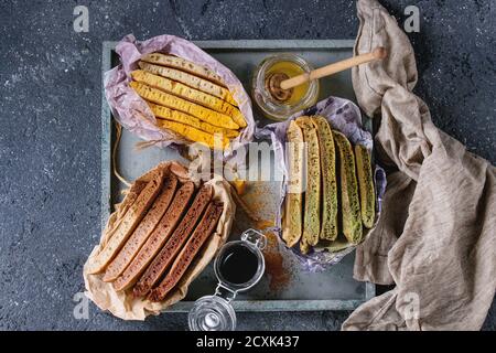 Varietà di fettine di american ombre cioccolato, tè verde Matcha e curcuma frittelle servita in carta involucro di carta con miele salse sul vassoio di legno su b Foto Stock