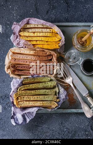 Varietà di fettine di american ombre cioccolato, tè verde Matcha e curcuma frittelle servita in carta involucro di carta con miele salse sul vassoio di legno su b Foto Stock