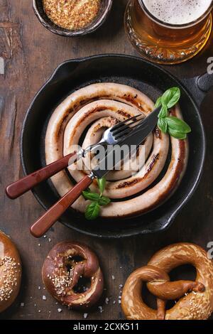 Bicchiere di birra chiara con salsicce fritte in padella con posate e tradizionali pretzel salati e la tazza di mostarda di oltre il vecchio legno scuro dello sfondo. Top vi Foto Stock