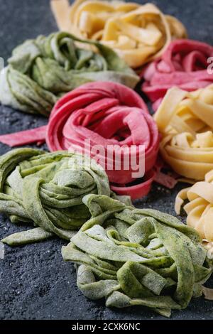 Varietà di tagliatelle di pasta fresca cruda fatte in casa, tagliatelle spinaci verdi, barbabietole rosa e giallo tradizionale su fondo di cemento scuro. Foto Stock