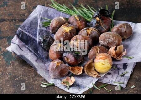Castagne arrostite nelle ceneri con rosmarino su carta su vecchio fondo di legno di tessitura scura. Primo piano con spazio per il testo. Foto Stock