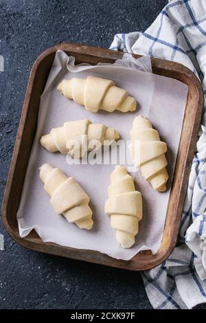 Materie crudi croissant sulla carta da forno nel vecchio forno il vassoio con carta asciugatutto per black texture di sfondo di calcestruzzo. Vista superiore Foto Stock