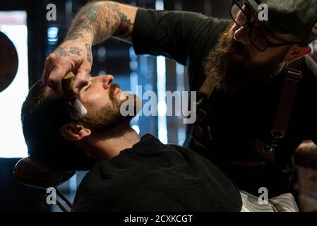 Parrucchiere che applica la schiuma da barba sulla barba del cliente Foto Stock