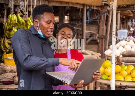 giovane uomo con un computer portatile che mostra qualcosa a una donna in un mercato africano locale Foto Stock