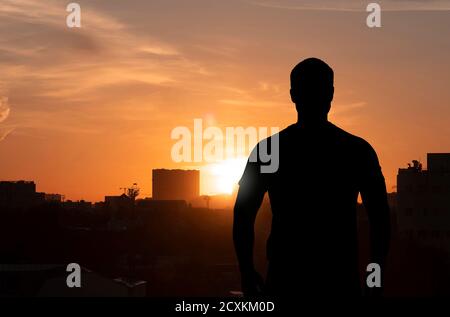 Silhouette di un uomo in piedi sulla cima dell'edificio di fronte alla città durante il tramonto, immagine concettuale Foto Stock