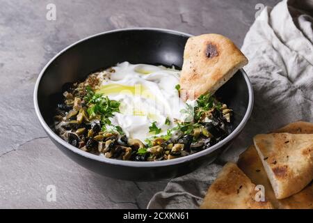 Labneh Middle Eastern libanesi di crema di formaggio dip con olio d'oliva, sale, erbe aromatiche, olive tapenade servito in tazza nera con il tradizionale pane pita su gra Foto Stock