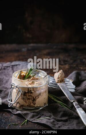 Vasetto di vetro di pata di fegato di pollo fatta in casa con grano di melograno e rosmarino, servito con coltello vintage su napkun tessile grigio su fondo di tessuto scuro Foto Stock