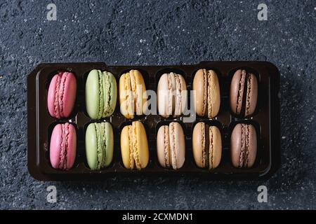 Varietà di colorati macaron dolci francesi da dessert con diversi ripieni in scatola di plastica di balck su sfondo di pietra scura. Vista dall'alto w Foto Stock