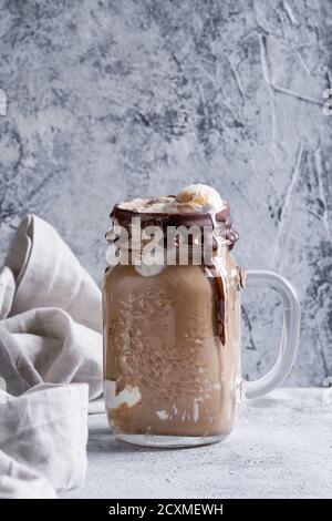 Frullato di caffè al cioccolato con paletta per gelato servita in vasetto di vetro in muratura su fondo grigio. Dolce estivo Foto Stock