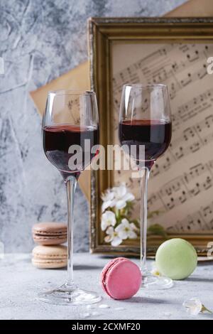 Due bicchieri di vino di porto con una varietà di colorati francesi macaron da dessert con diversi ripieni serviti con fiori primaverili e la vecchia musica no Foto Stock