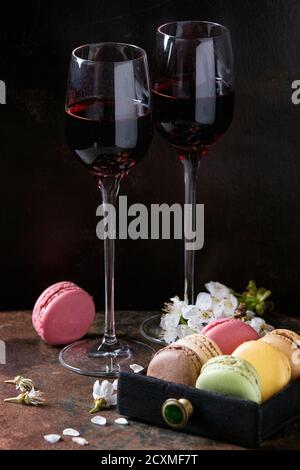 Due bicchieri di vino di Porto con una varietà di coloratissimi francese dessert dolci macaron amaretti con vari ripieni serviti con fiori di primavera oltre il buio Foto Stock