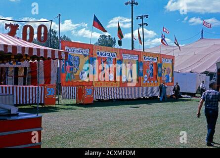 Una fotografia vintage del vicolo del sideshow a Clyde Beatty Cole Bros Brothers combinato Circus, USA c.1960. Le bandiere dipinte a mano indicano che le attrazioni includono elefanti, un mago, Frances Doran (un mago di spada), Celeste e Diablo (probabilmente un mangiatore di fuoco). Il materiale pubblicitario dipinto è ora considerato come arte popolare. Questa immagine è da un vecchio amatoriale americano Kodak trasparenza colore. Foto Stock