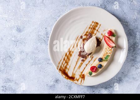 Dessert con piatti di banana biologica con frutti di bosco freschi, menta, riso al cioccolato e mousse di banana serviti con salsa balsamica su piatto bianco sopra la tex grigia Foto Stock