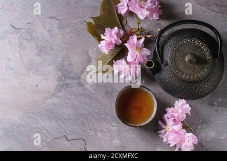 Nero teiera in ferro e ceramica tradizionale tazza di tè con il fiore fiori di colore rosa ciliegia ramo grigio Sfondo texture. Vista da sopra con lo spazio, Asiatica Foto Stock