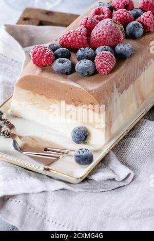 Tre strati di vaniglia, caffè e cioccolato torta gelato, servita con frutti di bosco surgelati e amaretti biscotti di forma rettangolare sulla piastra bianca, napki tessili Foto Stock