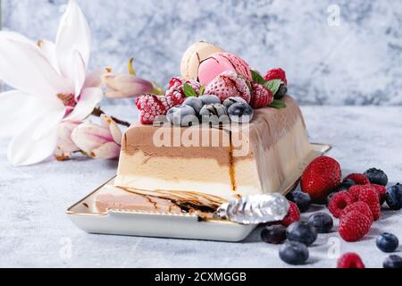 Tre strati di vaniglia, caffè e cioccolato torta gelato, servita con frutti di bosco surgelati e amaretti biscotti di forma rettangolare sulla piastra bianca, napki tessili Foto Stock