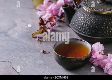 Nero teiera in ferro e ceramica tradizionale tazza di tè con il fiore fiori di colore rosa ciliegia ramo grigio Sfondo texture. Stile asiatico. Foto Stock