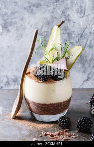 La prima colazione dolce a strati semi di Chia, budino di cioccolato, farinata di riso in vetro decorato da una fresca di more, Fette di pera, cacao in polvere. Con piedistallo Foto Stock
