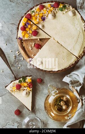 In casa fette di torta al cioccolato e pezzo di torta decorata da mango, lamponi, menta, il riso soffiato e fiori commestibili servita con vetro teiera su g Foto Stock