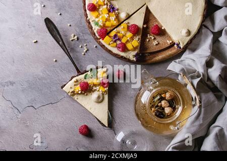 In casa fette di torta al cioccolato e pezzo di torta decorata da mango, lamponi, menta, il riso soffiato e fiori commestibili servita con vetro teiera su g Foto Stock