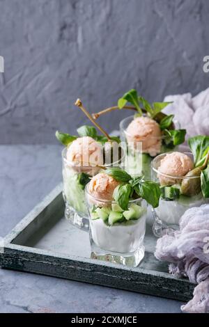 Verrines antipasto con salmone pate, caviale rosso, cetriolo, crema di formaggio, erbe, capperi in bicchieri serviti su legno su blu grigio Sfondo texture. Foto Stock