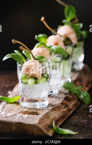 Verrines antipasto con salmone pate, caviale rosso, cetriolo, crema di formaggio, erbe, capperi in bicchieri serviti con rosa sale e basilico in legno che serve bo Foto Stock